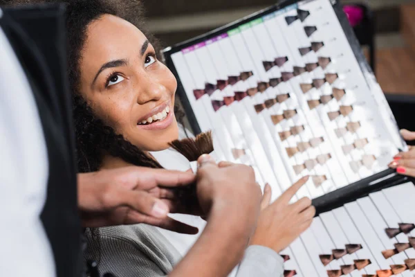 Mujer afroamericana señalando muestras de color de cabello sobre fondo borroso cerca del estilista - foto de stock