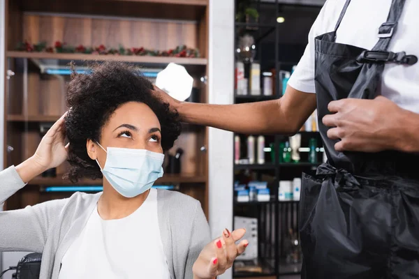 Femme afro-américaine en masque médical regardant coiffeur dans le salon — Photo de stock