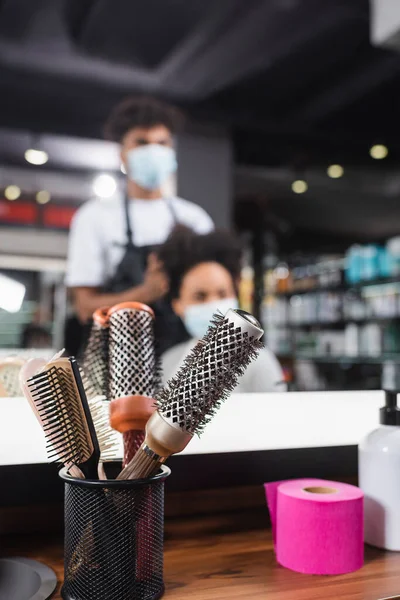 Brosses à cheveux et papier collier près du miroir et coiffeur flou travaillant avec le client — Photo de stock