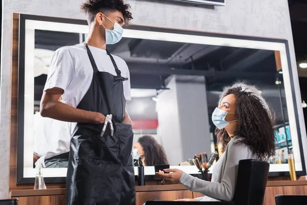African american client talking to hairdresser in medical mask in salon — Stock Photo
