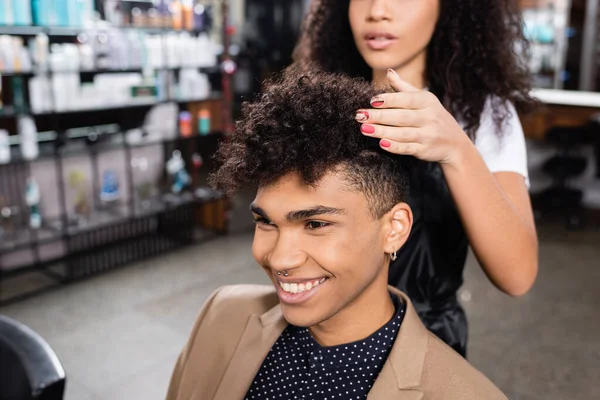 Client afro-américain positif regardant loin près du coiffeur dans le salon — Photo de stock