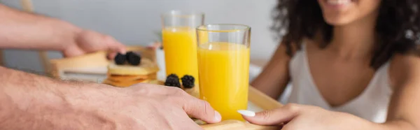 Partial view of man holding tray with breakfast near african american girlfriend on blurred background, banner — Stock Photo