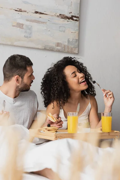 Bearded man looking at african american girlfriend eating blackberry — Stock Photo