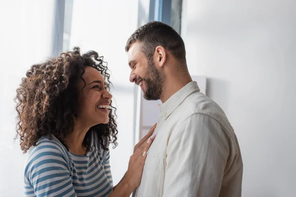 Heureux interracial couple sourire tout en étreignant à la maison — Photo de stock