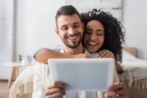 Fröhliches multiethnisches Paar blickt auf digitales Tablet — Stockfoto