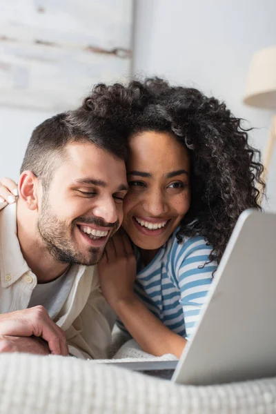 Positivo interracial casal refrigeração na cama e assistir filme no laptop — Fotografia de Stock