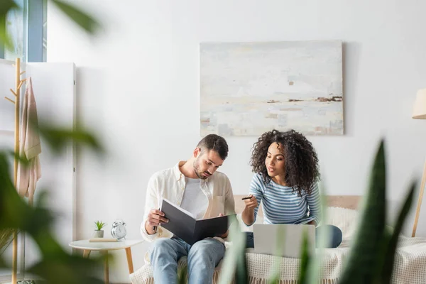 African american woman pointing at folder with taxes near boyfriend and laptop on bed — Stock Photo