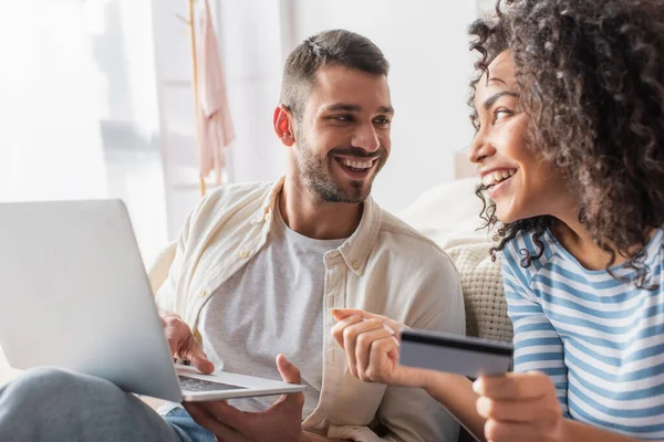 Feliz pareja interracial de compras en línea mientras se utiliza el ordenador portátil - foto de stock