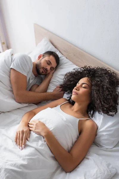 Vista de ángulo alto de pareja interracial durmiendo en la cama en casa - foto de stock