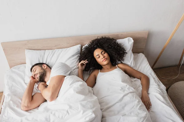 High angle view of multiethnic couple sleeping in bed at home — Stock Photo