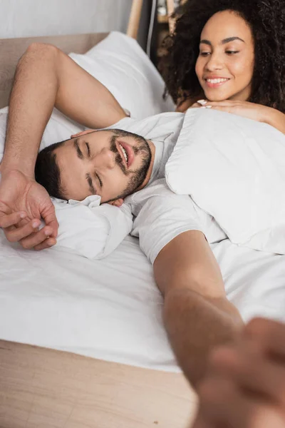 Happy african american woman looking at sleepy boyfriend in bed — Stock Photo
