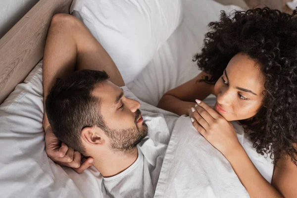 High angle view of happy african american woman looking at sleepy boyfriend in bed — Stock Photo