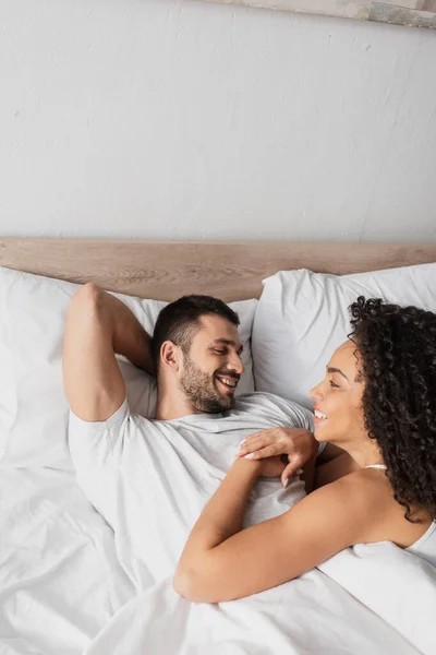 Feliz casal interracial olhando um para o outro na cama — Fotografia de Stock