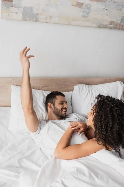 Alegre interracial pareja mirándose en la cama - foto de stock