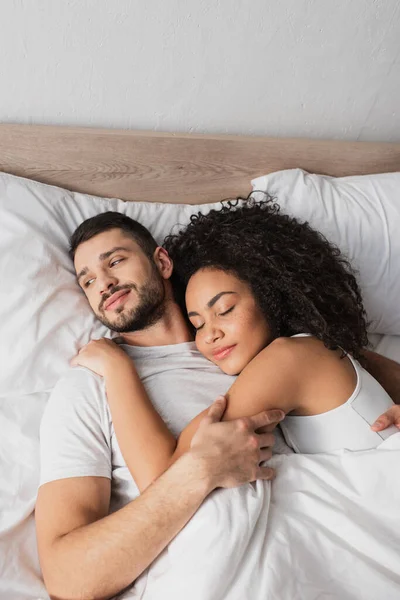 Alto ângulo vista de alegre interracial casal deitado na cama — Fotografia de Stock