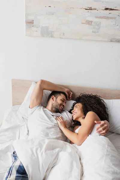 Позитивная межрасовая пара смотрит друг на друга, лежа в постели — стоковое фото