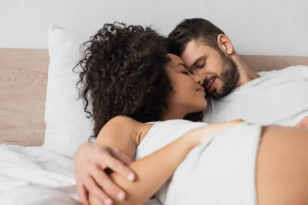 Cheerful interracial man and woman hugging while lying in bed — Stock Photo