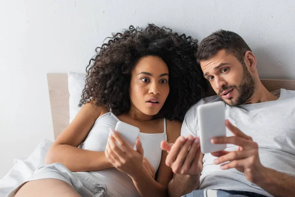 Impactado pareja interracial mirando el teléfono inteligente - foto de stock