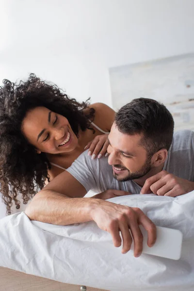 Hombre barbudo feliz sosteniendo teléfono inteligente cerca de la mujer afroamericana — Stock Photo