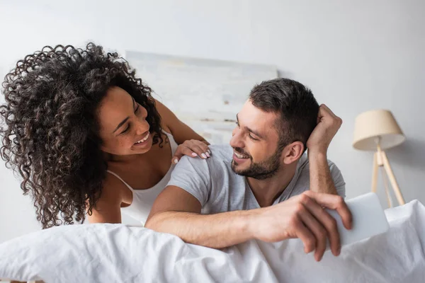 Hombre barbudo feliz sosteniendo teléfono inteligente cerca alegre mujer afroamericana - foto de stock