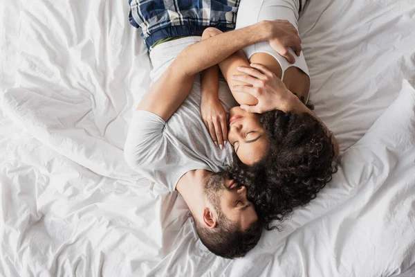 Vista superior do casal multiétnico abraçando e deitado na cama — Fotografia de Stock