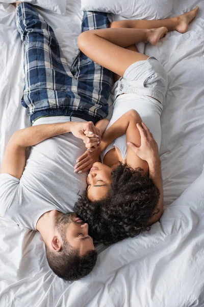 Vista superior do casal multiétnico abraçando e deitado na cama — Fotografia de Stock