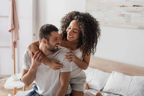 Rizado africano americano mujer abrazando positivo novio en dormitorio - foto de stock