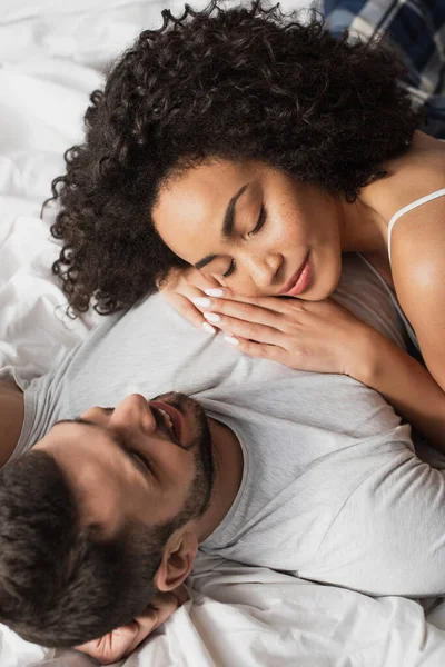 Alto ângulo vista de sorriso interracial casal deitado juntos na cama — Fotografia de Stock