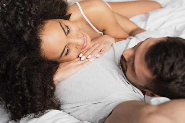 Happy interracial couple lying together on bed — Stock Photo