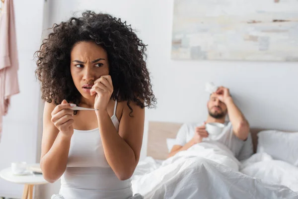 Worried african american woman holding digital thermometer near boyfriend on blurred background — Stock Photo