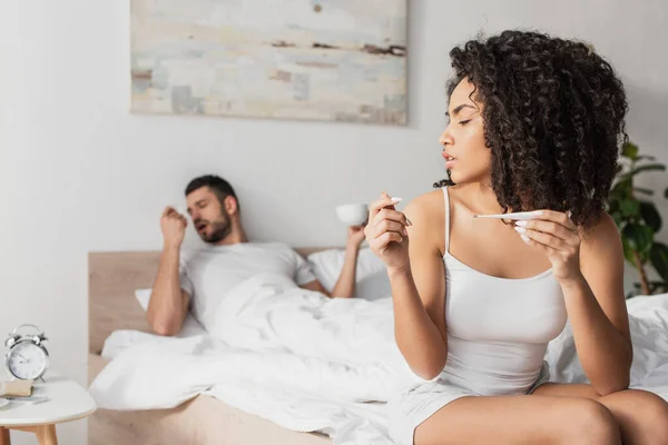 Sick african american woman holding digital thermometer near boyfriend on blurred background — Stock Photo