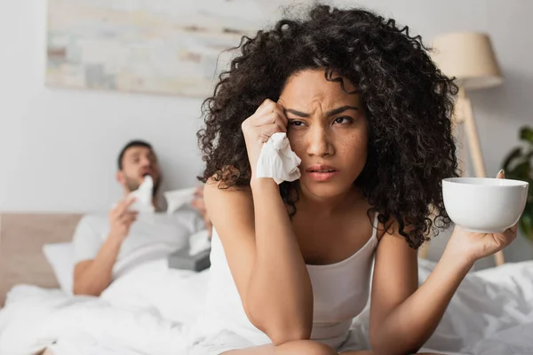 Sick african american woman holding tissue and cup near boyfriend on blurred background — Stock Photo