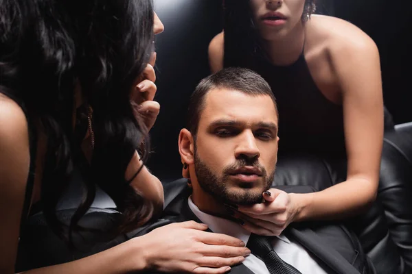 Femmes sensuelles séduire jeune homme d'affaires sur fond noir — Photo de stock