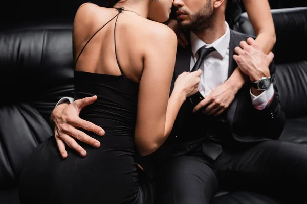 Teilweise Ansicht leidenschaftlicher Frauen küsst Mann auf Ledercouch isoliert auf schwarz — Stockfoto
