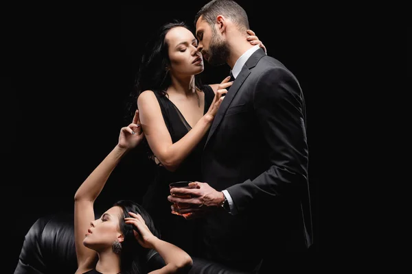 Apasionada mujer sentado cerca amantes besos aislado en negro - foto de stock