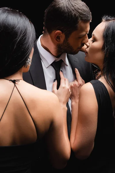 Mulheres morenas sedutoras perto de empresário em terno isolado em preto — Fotografia de Stock