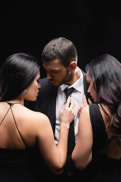 Élégant, brune femmes près de jeune homme en costume isolé sur noir — Photo de stock