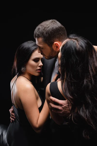 Joven hombre abrazando morena mujeres aislado en negro - foto de stock