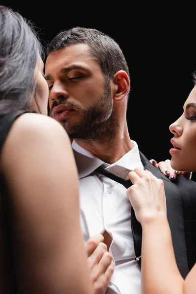 Femmes passionnées séduire jeune homme d'affaires isolé sur noir, flou premier plan — Stock Photo