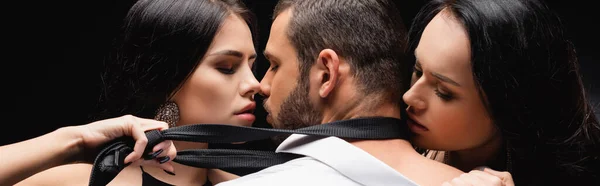 Sexy, morena mujeres desnudando hombre de negocios aislado en negro, bandera - foto de stock