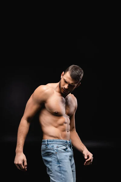 Sin camisa, hombre musculoso en jeans posando sobre fondo negro - foto de stock