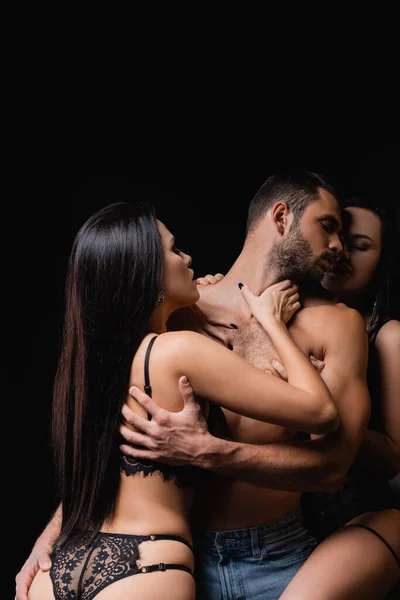 Sexy mulheres no renda lingerie seduzindo sem camisa homem isolado no preto — Fotografia de Stock