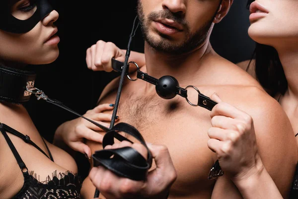 Cropped view of hot women with gag and flopping whip near shirtless man isolated on black — Stock Photo