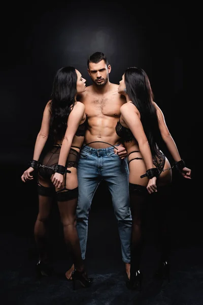 Full length view of shirtless man with flogging whip neat handcuffed women on black — Stock Photo