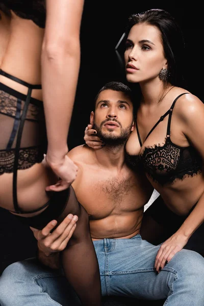 Sexy uomo abbracciare seducente donne mentre seduto isolato su nero — Foto stock