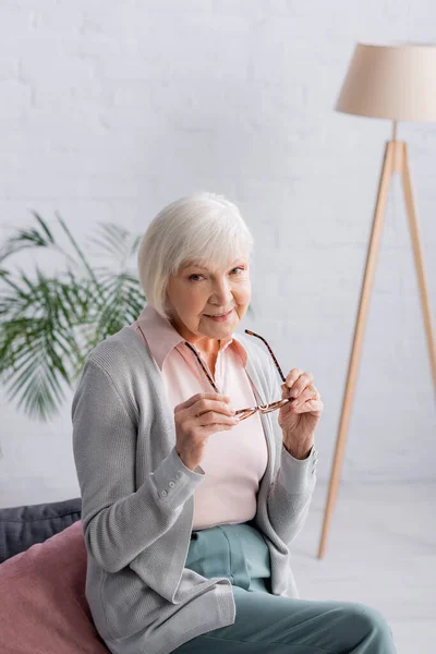 Senior woman holding eyeglasses and looking at camera — Stock Photo