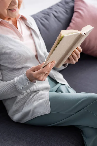 Обрізаний вид книги в руках усміхненої старшої жінки — стокове фото