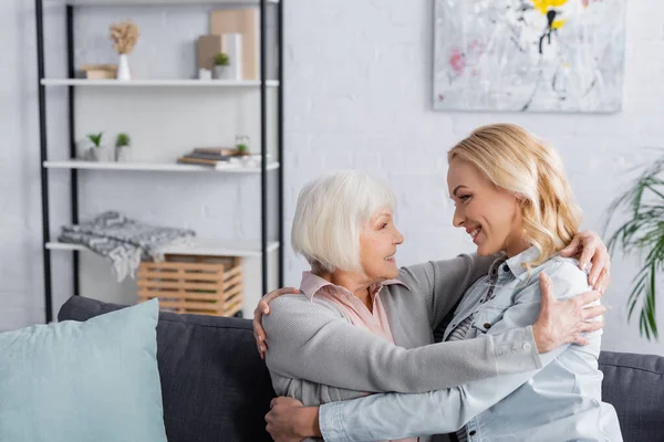 Mujer sonriente abrazando a la anciana madre en casa - foto de stock