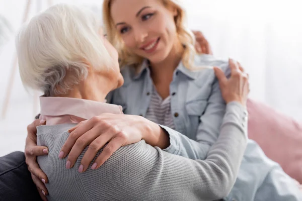 Femme âgée étreignant fille souriante sur fond flou — Photo de stock