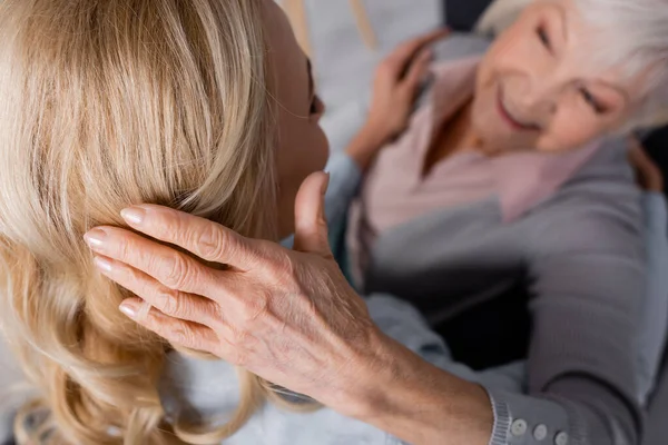 Senior woman on blurred background touching hair of daughter — Stock Photo